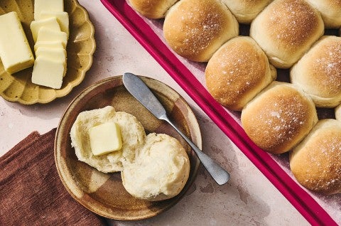 Big-Batch Quick Dinner Rolls on a sheet tray and one a plate with butter. - select to zoom