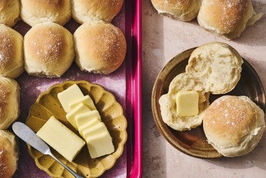 Big-Batch Quick Dinner Rolls on a baking sheet and two on a plate with butter.