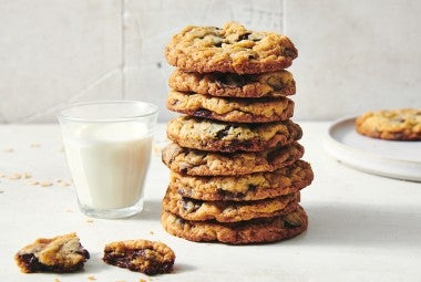 A stack of oatmeal chocolate chip cookies next to a glass of milk. The cookies have crisp golden brown edges and visible chocolate chips.