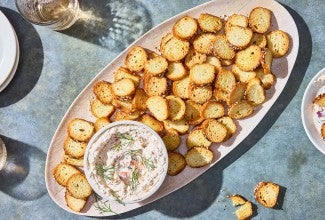 A platter of Everything Bagel Chips spread out around a small bowl of Smoked Salmon Cream Cheese dip.