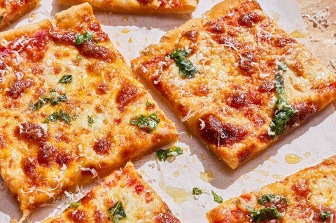 Slices of Gluten-Free Sheet Pan Pizza showing a classic cheesy pizza with brown bubbly cheese and drops of basil pizza topping. - select to zoom