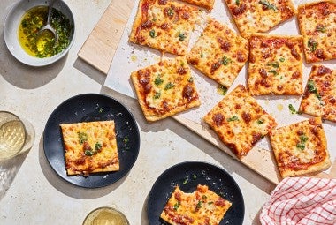 Slices of Gluten-Free Sheet Pan Pizza seen from above and randomly arranged on a cutting board with other slices on plates.