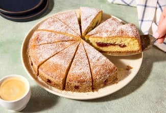 A hand removing a slice of Jelly Doughnut Cake from a plate. You can see the inside of the slice with a golden interior and lovely jelly filling.