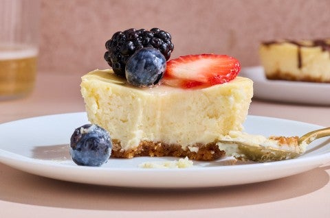 A Mini Cheesecake on a plate seen from the side showing a smooth interior and short-crust on the bottom with fresh berries on top. - select to zoom
