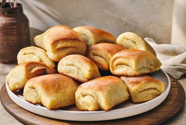 Parker house rolls stacked on a plate showing a buttery gloss and perfect folded bake.