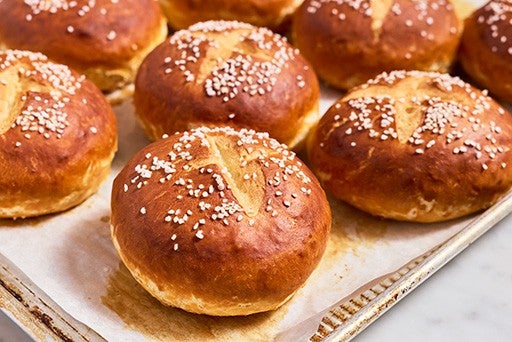 Freshly baked pretzel buns on a sheet tray.