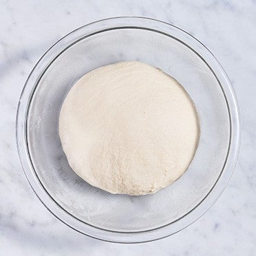 Pretzel bun dough in a clear glass bowl.