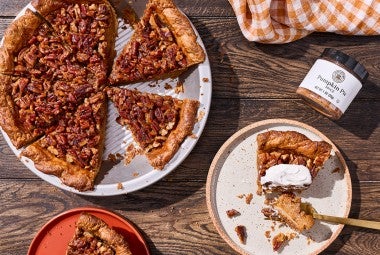 Looking at a rustic table with a pumpkin pecan pie slice and served on a plate, topped with whipped cream.