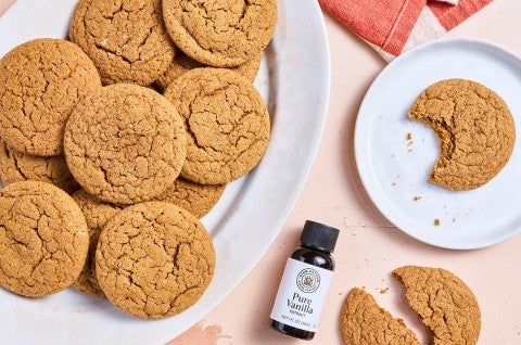 Soft Brown Sugar Cookies spread out on various plates with a small jar of King Arthur Baking Vanilla Extract. - select to zoom