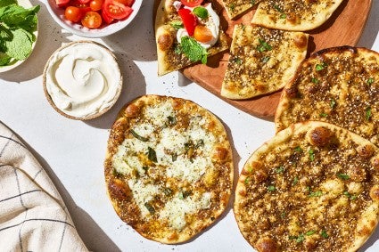 Za’atar Manakeesh spread out with toppings, dip, herbs, and veggies.